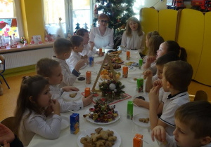 Pani dyrektor Maria Królikowska, pani Ewa Janicka oraz dzieci jedzą słodki i owocowy poczęstunek.